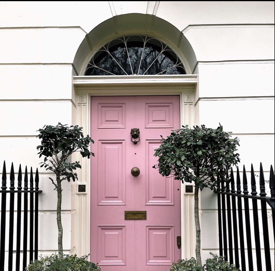 Fachada blanca con puerta rosa y jardineras
